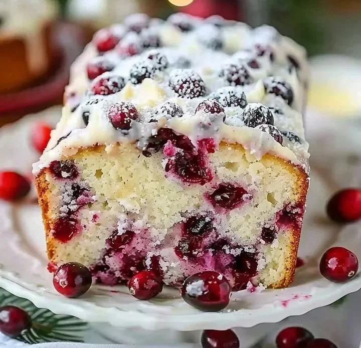 Sliced Christmas Cranberry Pound Cake on a festive plate with cranberries and greenery.