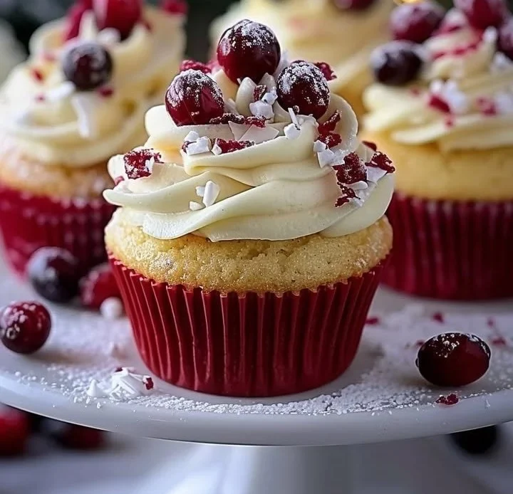 Cranberry orange cupcakes topped with white chocolate frosting on a decorative plate.