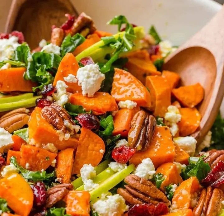 Colorful roasted sweet potato salad with greens and dressing served in a bowl.
